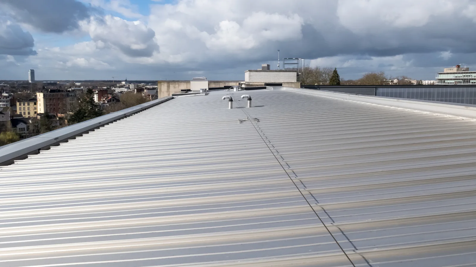 Metal commercial roof with raised vents and buildings beyond