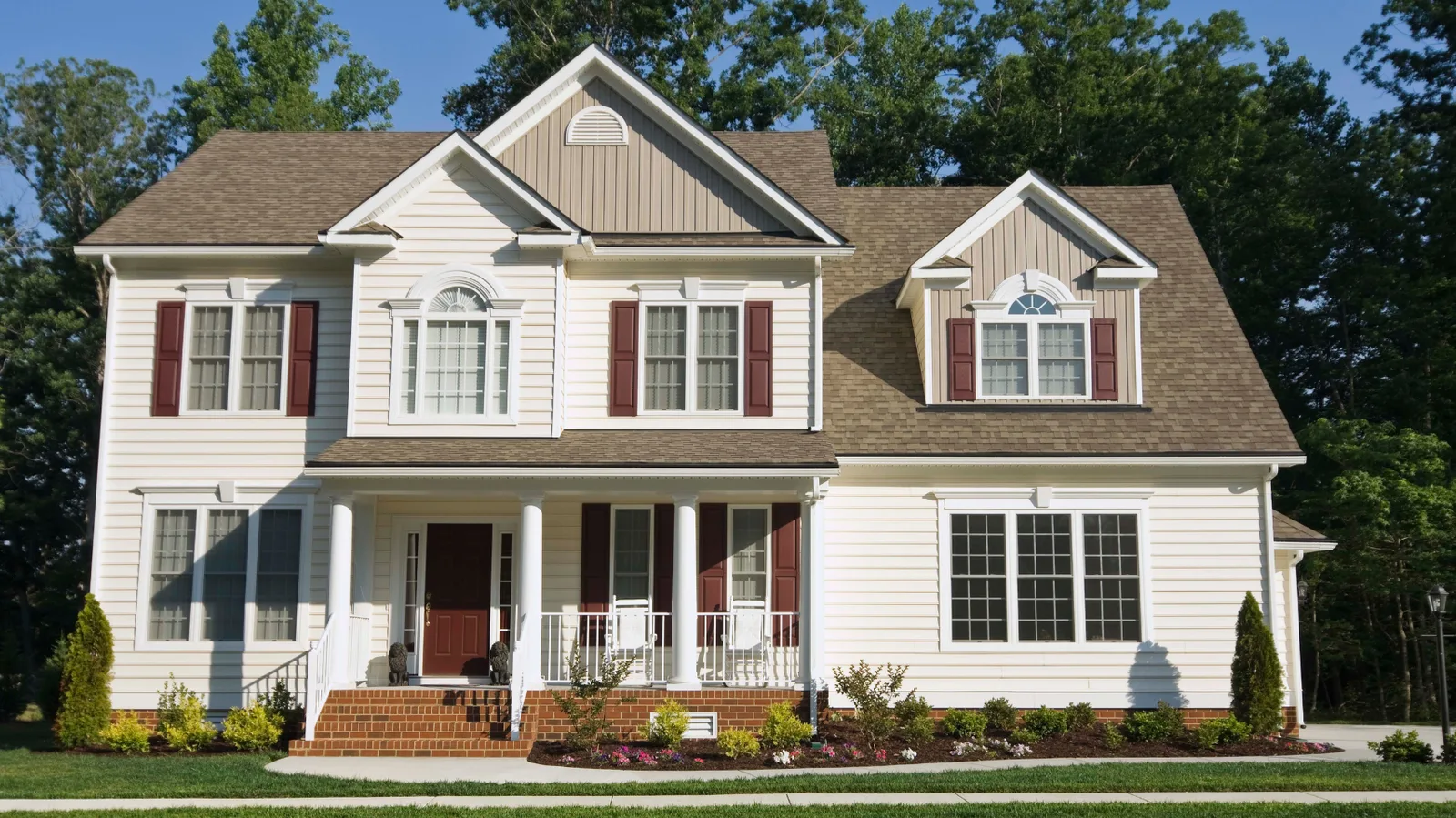 Cream two-story house with a brown shingle roof and covered porch