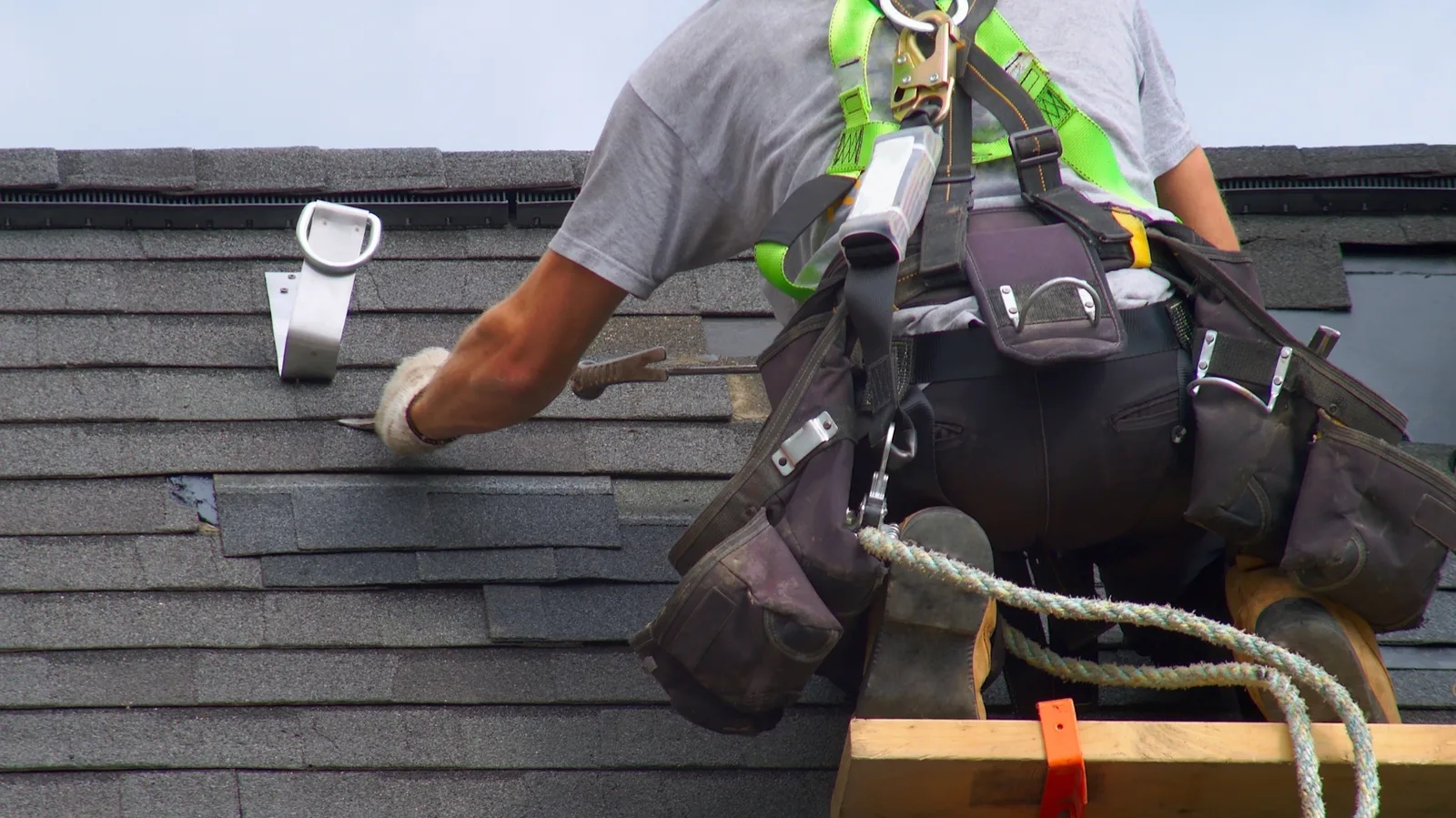 A roofer secured with a safety harness working on asphalt shingles